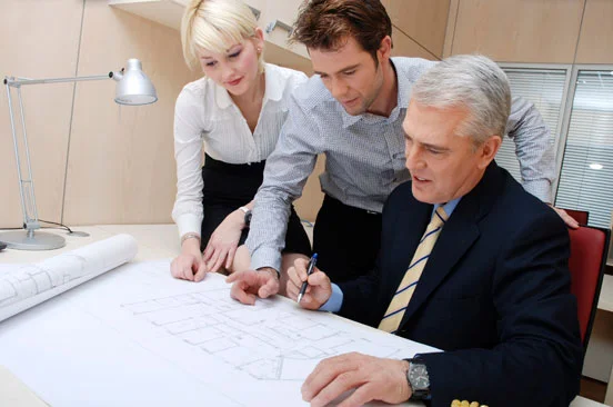 three people in business attire looking at blueprints